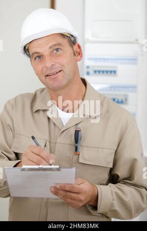 Konzentrierter Mann Baumeister im Helmbau Schreiben auf Zwischenablage Stockfoto