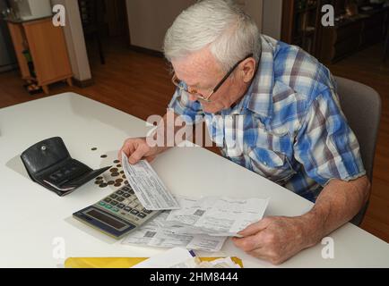 Älterer Mann, der am Tisch sitzt und die Finanzen berechnet. Alter Mann, der Rechnungen überprüft. Mann, der Münzen auf dem Tisch zählt. Pensionsberechnungskonzept Stockfoto