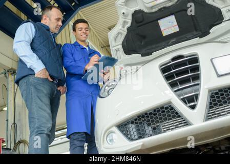 Lehrling Mechaniker, der Auto unter Aufsicht inspiziert Stockfoto