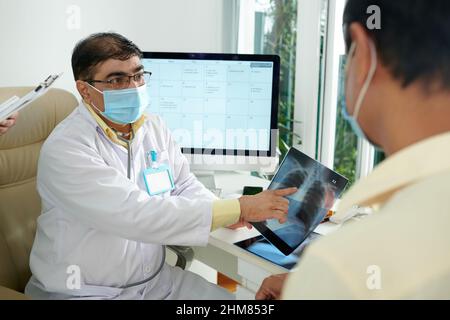 Arzt, der einem älteren Patienten eine Röntgenaufnahme der Lunge mit einem verdächtigen Lungenknoten zeigt Stockfoto