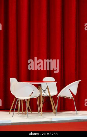 Moderner Tisch und Stühle mit rotem Vorhang im Hintergrund. Stilvolles Innenraumdasein Stockfoto