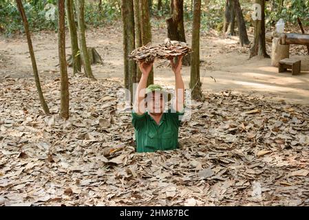 Ein Reiseleiter zeigt einen versteckten Eingang zum Tunnelnetz im Cu Chi Tunnel Complex, Cu Chi Bezirk, Südvietnam Stockfoto