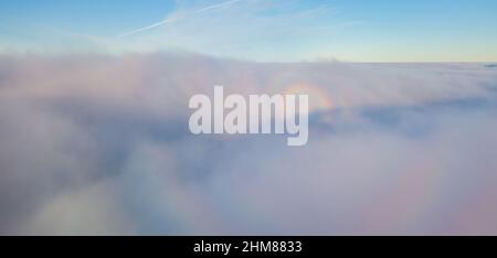 Drohnenflug über den Nebel. Unten sind dicke Nebelwolken, die Sonne bricht durch die Wolken. Stockfoto