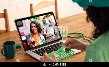 Kaukasische Frau, die eine Schamrock-Brille hält, während sie zu Hause einen Videoanruf auf dem Laptop führt Stockfoto