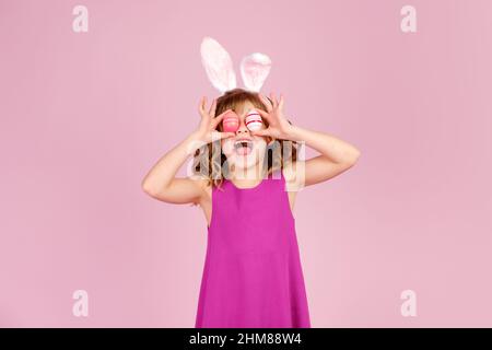 Entzücktes Kind, das während der Osterparty im pinken Studio das Auge mit Eiern bedeckte Stockfoto