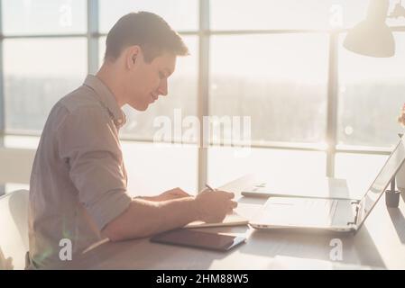 Freier Mann schreibt zu Hause oder im Büro auf einem Notebook Stockfoto