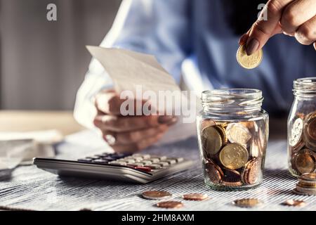 Detail einer Frau, die eine Rechnung in einer Hand hält und fünfzig Cent in ein Glas mit Rechner auf dem Tisch legt. Stockfoto