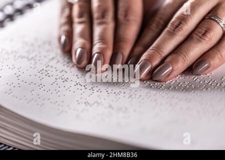 Detail der weiblichen Hände eines blinden Lesers, der das in Braille-Schrift gefertigte Buch berührt. Stockfoto