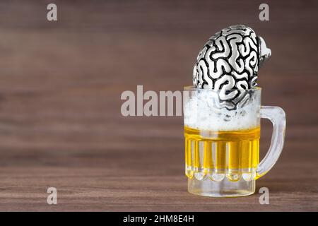 Anatomische Stahlkopie eines menschlichen Gehirns in einem Miniatur-Bierkrug vor einem hölzernen Hintergrund. Ertrinkende Trauer und Probleme im Alkohol. Stockfoto