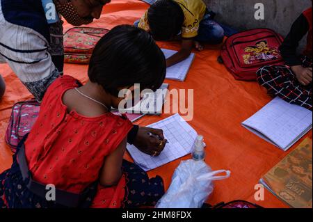 Nabin Nagar, Westbengalen, Indien. 7th. Februar 2022. Die Regierung des Bundesstaates Westbengalen hat am 7th. Februar „˜Paray Shikshalaya“ ins Leben gerufen, Eine gemeindebasierte Schularbeit in Nachbarschaften, die sich an Grundschüler richtet, um die programmierten Ziele zu erreichen, besteht darin, einen großen Teil der Schüler zurückzuholen, die in den letzten zwei Jahren aufgrund der Schließung von Schulen aufgrund von Covid-19 aus dem formalen Bildungssystem ausgefallen sind. Die Vorschulklasse einer an der Grenze zwischen Indien und Bangladesch angrenzenden Grundschule wird auf einer leeren Straße neben dem Zaun bei Nabin Nagar durchgeführt, es kommen gelegentlich Haustiere. (Kredit Stockfoto