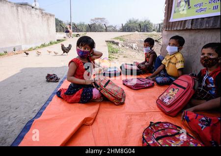 Nabin Nagar, Westbengalen, Indien. 7th. Februar 2022. Die Regierung des Bundesstaates Westbengalen hat am 7th. Februar „˜Paray Shikshalaya“ ins Leben gerufen, Eine gemeindebasierte Schularbeit in Nachbarschaften, die sich an Grundschüler richtet, um die programmierten Ziele zu erreichen, besteht darin, einen großen Teil der Schüler zurückzuholen, die in den letzten zwei Jahren aufgrund der Schließung von Schulen aufgrund von Covid-19 aus dem formalen Bildungssystem ausgefallen sind. Die Vorschulklasse einer an der Grenze zwischen Indien und Bangladesch angrenzenden Grundschule wird auf einer leeren Straße neben dem Zaun bei Nabin Nagar durchgeführt, es kommen gelegentlich Haustiere. (Kredit Stockfoto