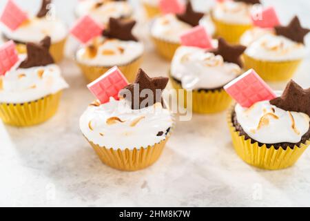 Gourmet-S'mores-Cupcakes mit Meringue-Zuckerguss und garniert mit sternförmiger Schokolade graham Cracker und einer pinken Mini-Tafel Schokolade. Stockfoto