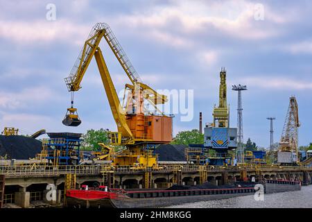 Nahansicht von Hafenkränen mit Clamshell oder Greifer, die Kohle laden, um Boote oder Lastkähne am bewölkten Tag zu schleppen. Energie, Mineralien, Umwelt Stockfoto