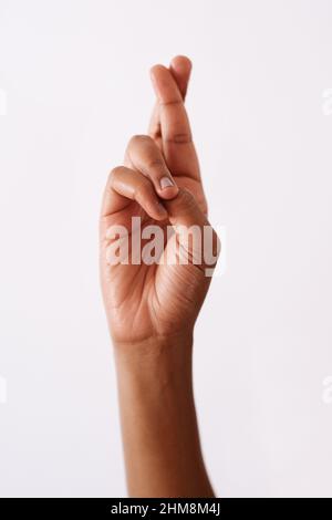 Ich drücke mir die Daumen. Studioaufnahme einer nicht erkennbaren Frau, die die Daumen vor einem weißen Hintergrund drückt. Stockfoto