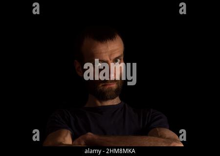Ein ernsthafter Mann auf dunklem Hintergrund in einem dunklen T-Shirt hält seine Hände vor sich. Platz für Text Stockfoto
