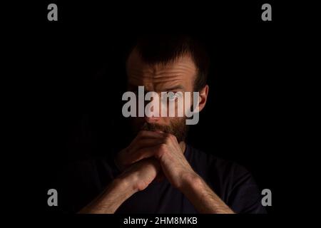 Ein Mann mittleren Alters, in einem dunklen T-Shirt, posiert mit gekreuzten Armen. Isoliert auf einem dunklen Hintergrund. Stockfoto