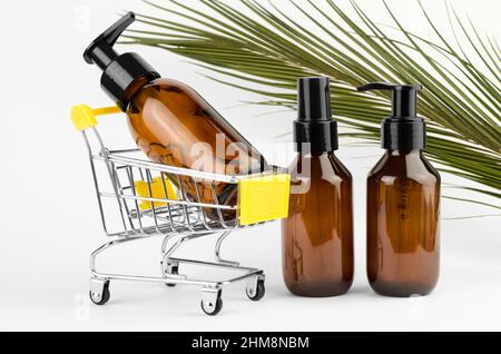 Kosmetikflaschen mit Spender auf weißem Hintergrund mit Palmblatt. Kosmetikflasche in einem Warenkorb. Spa-Produkte Stockfoto