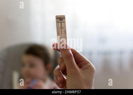 Schnelltest mit positivem Corona-Antigen in der Hand mit Kind im Hintergrund. Test- und Impfkonzept für Kinder, Kinder Stockfoto