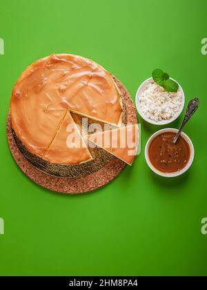 Klassischer Käsekuchen mit gesalzenem Karamell auf grünem Hintergrund. Hausgemachtes, köstliches Gebäck. Süßes Dessert. Vertikale Aufnahme. Speicherplatz kopieren Stockfoto