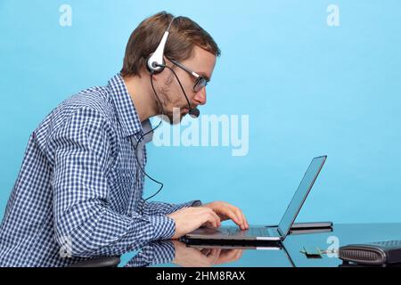 Seitenansicht Porträt eines ernsthaften Mannes, eines professionellen IT-Programmierers, eines Callcenter-Bedieners, der mit einem Laptop arbeitet, der auf blauem Hintergrund isoliert ist Stockfoto