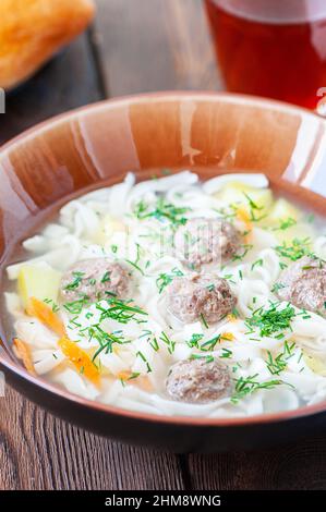 Hausgemachte Fleischbällchen-Suppe mit Nudeln auf Holzboden. Nahaufnahme. Stockfoto