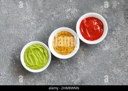 Verschiedene Saucen, französischer Senf, Ketchup und Guacamole auf grauem Hintergrund. Draufsicht. Stockfoto