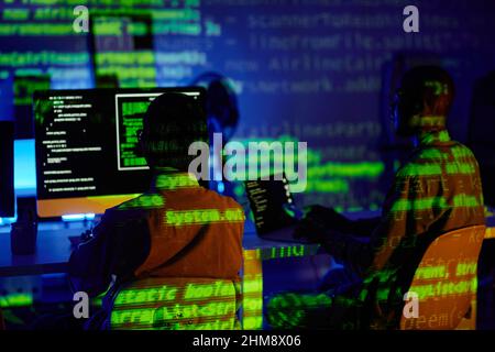 Rückansicht von zwei jungen interkulturellen Programmierern, die an Schreibtischen vor Computern sitzen und an neuer Software arbeiten Stockfoto