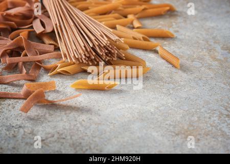 Drei Arten von Vollkorn-Pasta, Tagliatelle, Spaghetti und Penne rigate, rustikalen grauen Stein Hintergrund mit Kopierer Platz, gesunde Nudel Alternative Co Stockfoto