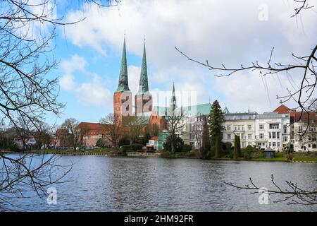 Lübecker Dom mit zwei Türmen in historischer Backsteinarchitektur, berühmtes Wahrzeichen hinter dem idyllischen Mühlenteich, wolkig blauer Himmel, Kopierfläche, ausgewählte f Stockfoto