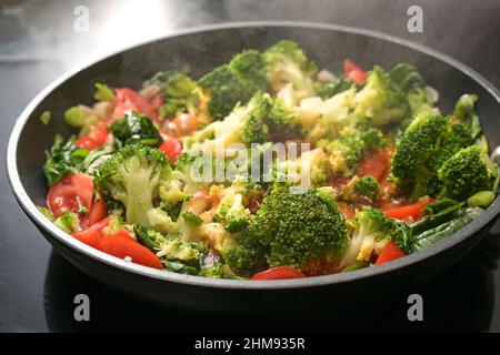 Rotes und grünes Gemüse in einer Pfanne mit Brokkoli, Tomaten, Frühlingszwiebeln und Spinat auf dem Herd dampfen und vegetarische Gerichte für eine gesunde Ernährung zubereiten Stockfoto