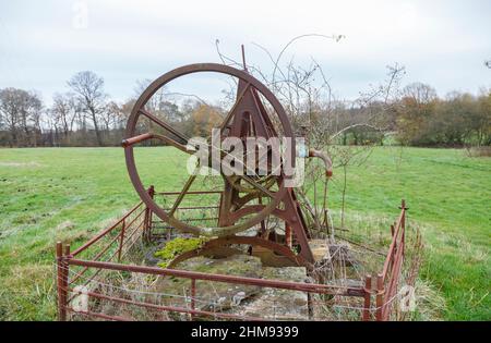 Alte Zahnräder und Räder aus nicht mehr genutzten, rostenden landwirtschaftlichen Maschinen, eine Brunnenwasserpumpe, die im Winter auf einem Feld in Vann, in der Nähe von Ockley, Surrey, steht Stockfoto