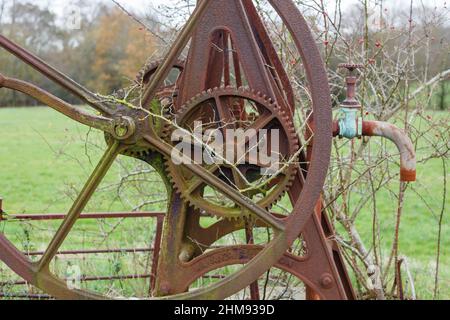 Alte Zahnräder und Räder aus nicht mehr genutzten, rostenden landwirtschaftlichen Maschinen, eine Brunnenwasserpumpe, die im Winter auf einem Feld in Vann, in der Nähe von Ockley, Surrey, steht Stockfoto