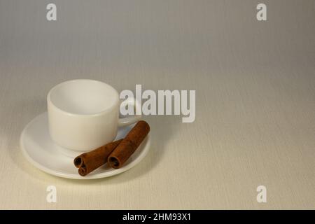 Leere Kaffeetasse aus weißem Porzellan und Zimtstangen auf hellem Hintergrund. Stockfoto