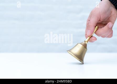 Hand hält eine goldene Glocke auf dem weißen Hintergrund, Kopierraum, Concept School, Teather oder Manager im Hotel. Stockfoto