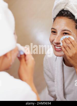 Ich kenne ein paar Tricks, wenn es darum geht, makellose Haut zu erreichen. Aufnahme einer schönen jungen Frau, die in den Spiegel schaut, während sie ihr Gesicht putzt. Stockfoto