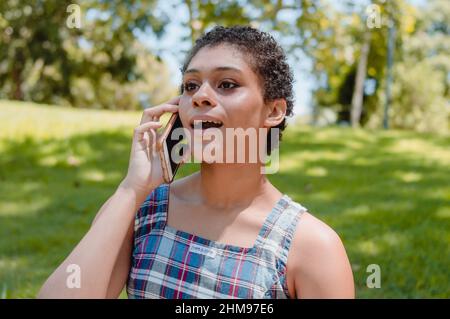 Schöne junge Brünette hispanic latina argentinischen Mädchen mit kurzen Haaren lächeln mit ihrem Mund offen aufgeregt Kommunikation durch das Telefonieren in Stockfoto