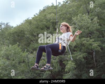 Russland, Sotschi 05.09.2021. Ein fröhliches Mädchen, das am Seil hängt, fliegt in den Bergen durch die Luft. Zipline Stockfoto