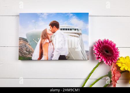 Leinwanddruck mit Galerie Wrap Technik auf weißem Holztisch, Draufsicht. Hochzeitsfoto und Blumenstrauß von Gerbera Blumen. Gestreckte Fotografie. Portrai Stockfoto