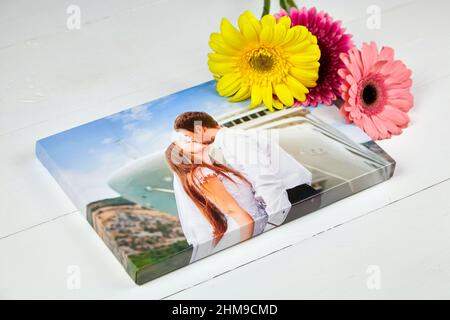 Leinwanddruck mit Gallery Wrap-Technik auf weißem Holztisch. Hochzeitsfoto und Strauß von Gerbera Blumen. Gestreckte Fotografie, Porträt eines kis Stockfoto