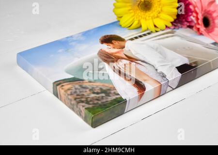 Leinwanddruck mit Gallery Wrap-Technik auf weißem Holztisch. Hochzeitsfoto und Strauß von Gerbera Blumen. Gestreckte Fotografie, Porträt eines kis Stockfoto