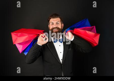 Glücklicher Mann in Smoking Fliege mit Business-Belohnung in Einkaufstaschen. Anlass Gruß. Stockfoto