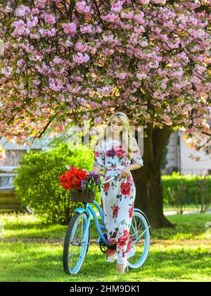 Frühlingsferien. Frau mit Tulpenstrauß. Sakura-Baum blüht. Mädchen langes Kleid Retro Cruiser Fahrrad Sakura Baum. Sakura-Saison. Romantische Fahrradtour Stockfoto
