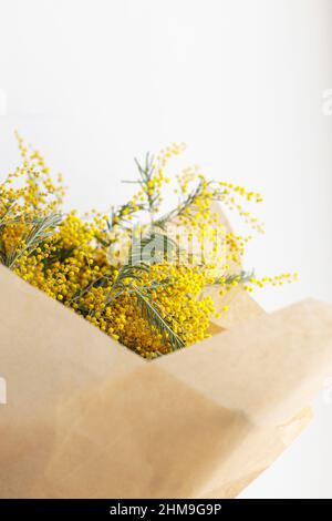 Stilvolles Mimosa Bouquet auf weißem Hintergrund. Glücklicher Frauentag und glücklicher Muttertag. Wunderschöne Mimosenblumen in Bastelpapier in der Nähe des Fensters. 8 ma Stockfoto