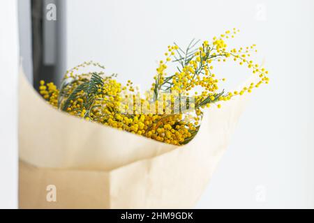 Stilvolles Mimosa Bouquet auf weißem Hintergrund. Glücklicher Frauentag und glücklicher Muttertag. Wunderschöne Mimosenblumen in Bastelpapier in der Nähe des Fensters. 8 ma Stockfoto