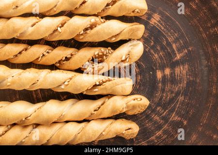 Grissini-Brotstäbchen mit Sesamsamen auf einer Tonplatte, Nahaufnahme, Draufsicht. Stockfoto