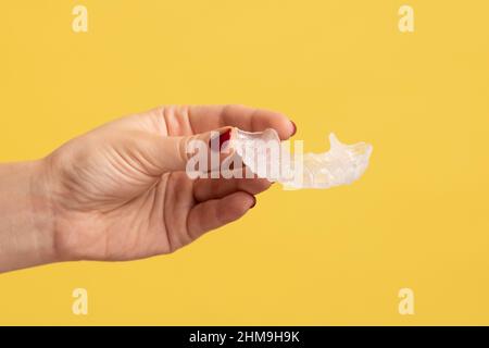 Nahaufnahme Profil Seitenansicht Porträt der Frau Hand hält Dental Aligner Halter in der Zahnklinik für schöne Zähne Behandlungskurs. Innenaufnahme des Studios isoliert auf gelbem Hintergrund. Stockfoto