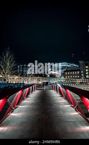 Brücke über den Regent's Canal, die zum Granary Square, Coal Drops Yard führt, alle nachts beleuchtet. Die Entwicklung der Gasinhaber ist im Hintergrund zu sehen. Stockfoto