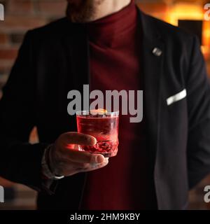 Red Negroni Cocktail mit einer Orangenschale in einem altmodischen Glas, das von einer Hand eines Mannes gehalten wird Stockfoto