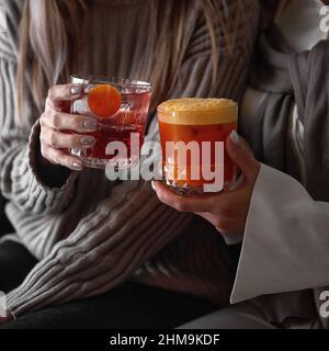 Nahaufnahme eines altmodischen Glases mit einem roten Cocktail in den Händen einer kuscheligen Frau Stockfoto