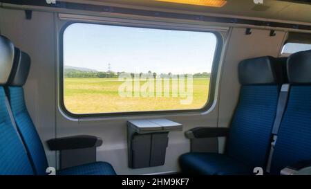 Der Zug fährt mit leeren Sitzen und die Landschaft ist am Fenster zu sehen Stockfoto